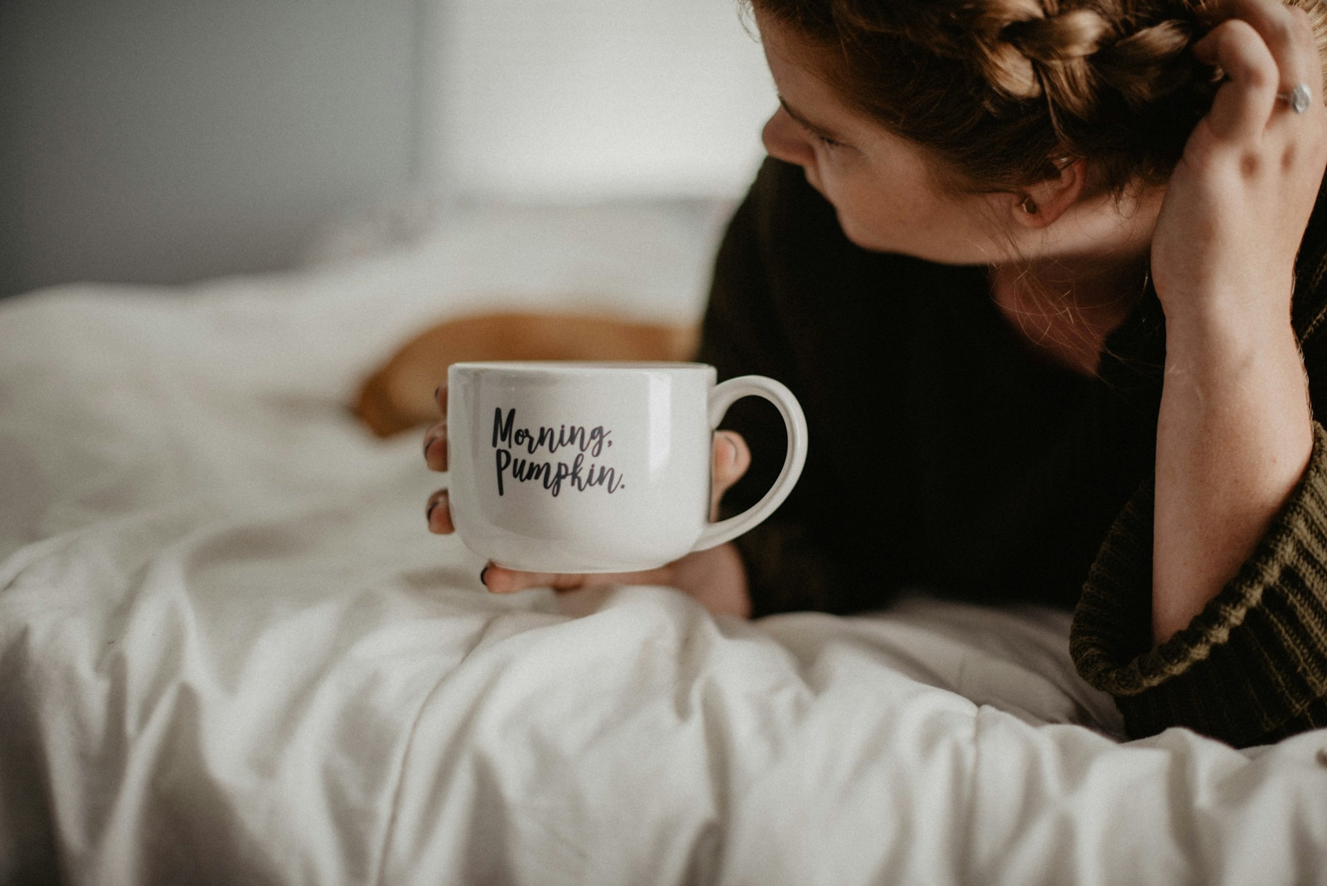 A woman lying on the bed with a mug in her hand